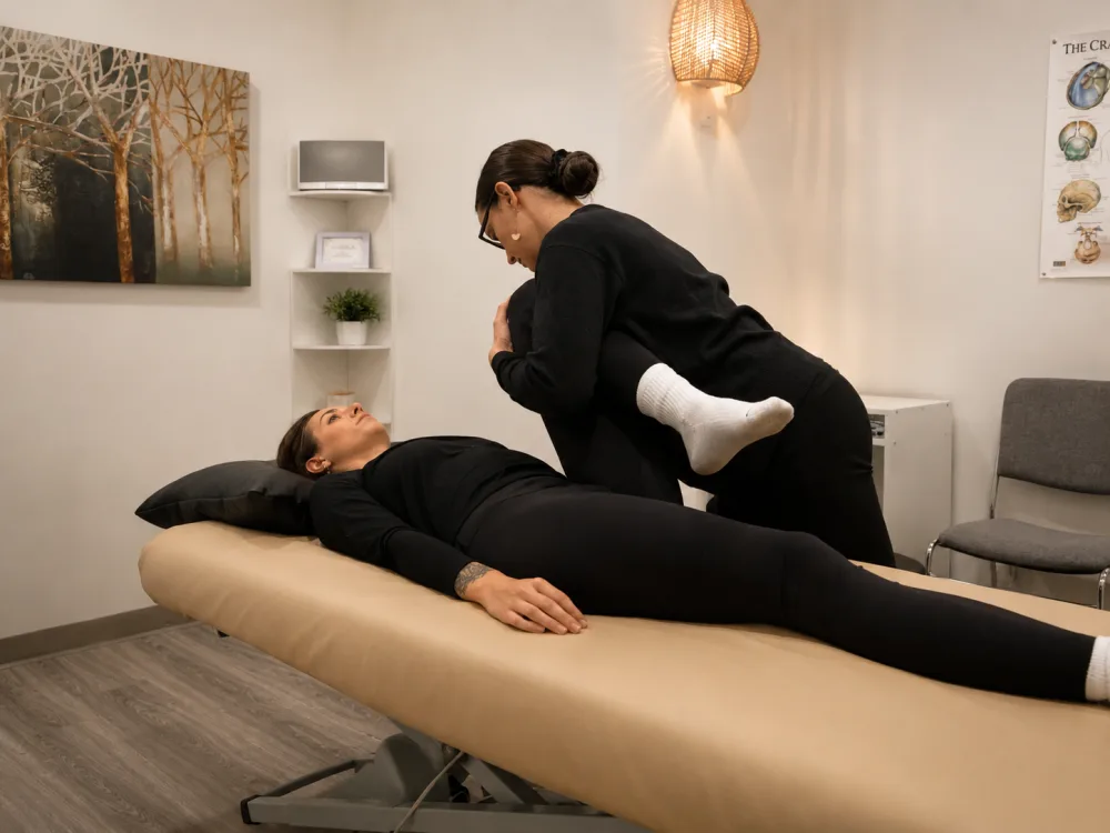 Bryhnn Freitas giving a hands-on hip and leg treatment to a client on the treatment table.